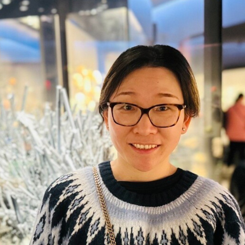 Smiling woman with glasses and dark hair wearing patterned sweater in shopping mall