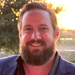 Sean Carver, smiling man with beard wearing blue jacket in outdoor setting with warm lighting
